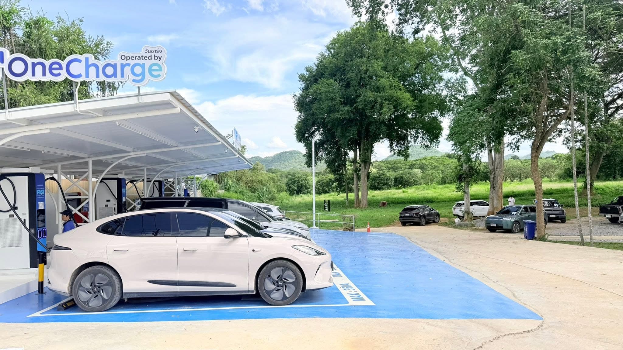 Wide view of the Fast Charge POW Pak Chong station with the Khao Yai hills in the background and an EV charging