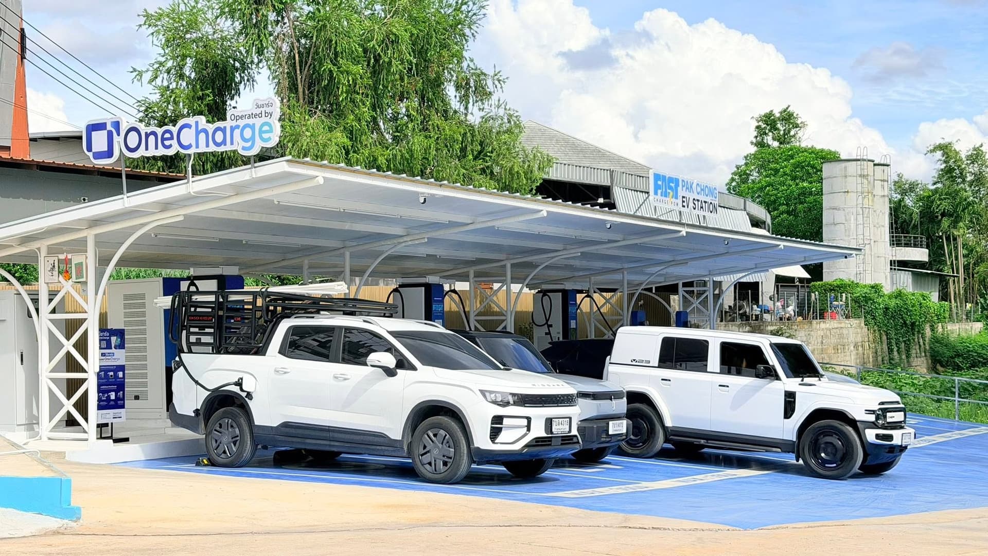 ป้าย OneCharge ที่สถานีชาร์จ Fast Charge POW ปากช่อง มีรถ EV หลายคันจอดชาร์จอยู่ใต้หลังคา